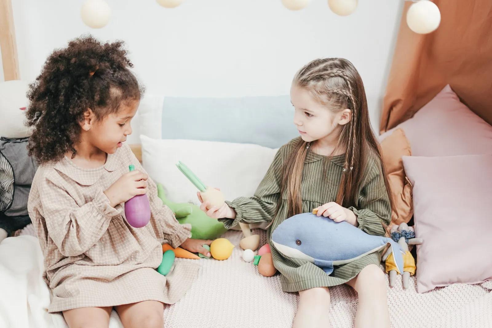 Two young girls enjoying a playful moment with plush toys in a cozy indoor setting.